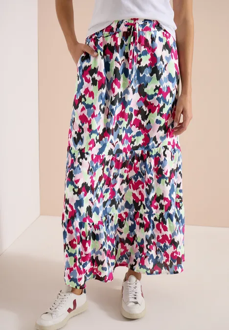 Jupe midi colorée à motifs floraux abstraits, coupe fluide, portée avec des baskets blanches.
