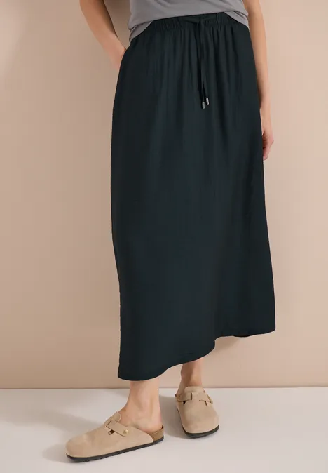 Zwarte maxirok met trekkoord, gecombineerd met beige mules.