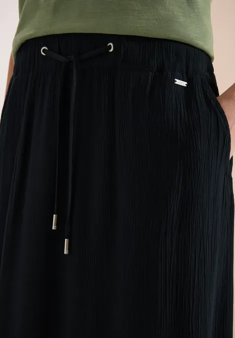 Schwarze plissierte Hose mit Kordelzug und seitlichen Taschen, kombiniert mit grünem Oberteil.