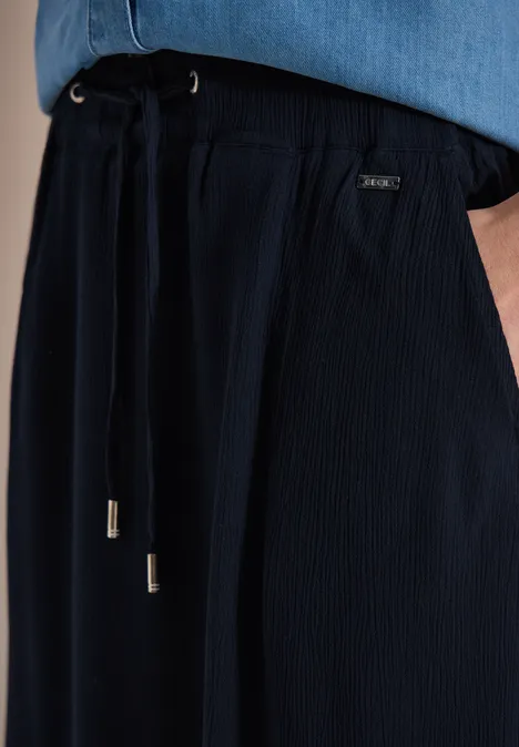 Nahaufnahme einer dunkelblauen Hose mit Kordelzug und kleinen Metallenden, getragen zu einem hellblauen Oberteil.