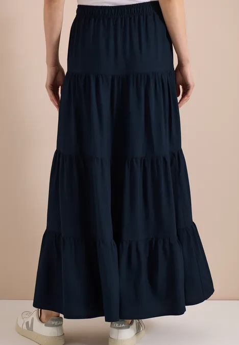 Rückenansicht eines langen, stufigen, dunkelblauen Maxirocks mit elastischem Bund und weißen Sneakern.