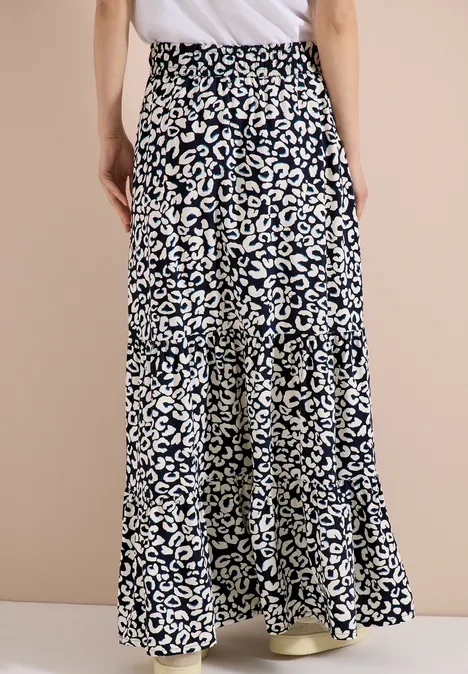 Rückansicht einer Person in weiten, blau-weiß gemusterten Hosen und hellen Sneakern vor schlichtem Hintergrund.