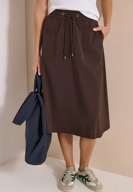 Bruine midirok met trekkoord en steekzakken, gecombineerd met witte sneakers en een donkerblauwe tas.