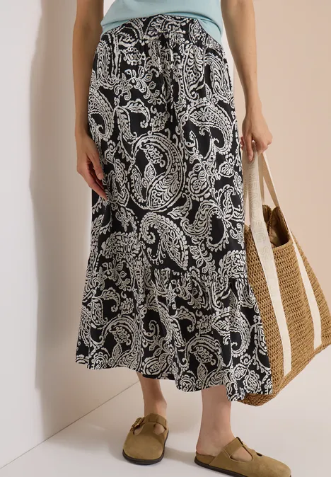 Jupe longue à motifs floraux Black Femme en jupe longue noire à motifs cachemire blancs, sac en paille et sandales brunes.