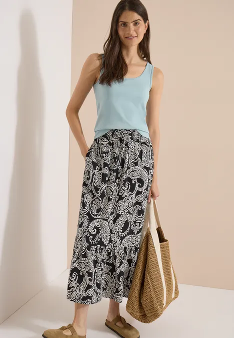 Jupe longue à motifs floraux Black Femme en débardeur bleu clair et jupe midi paisley noir et blanc, portant un grand panier en paille.