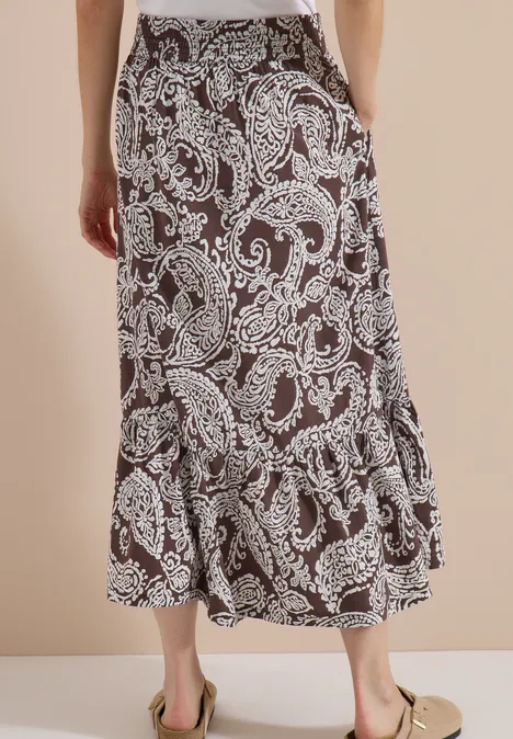 Jupe longue à motifs floraux brown cacao Jupe midi noire à motif cachemire blanc, volantée au bas, portée avec des mules beige.
