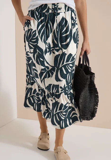 Jupe midi plissée crème à motif de larges feuilles vert foncé, ourlet asymétrique et sac noir tressé