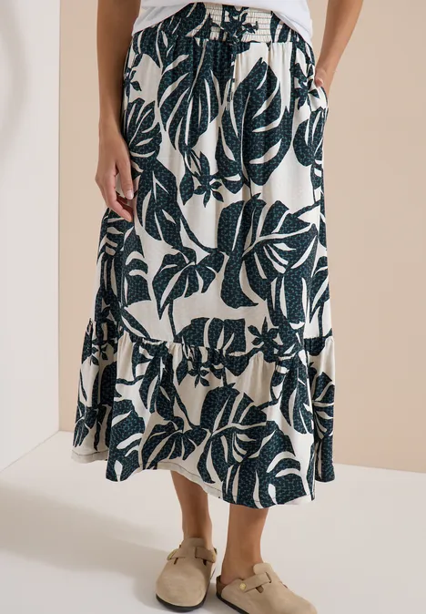 Jupe midi crème à imprimé grandes feuilles de monstera vert foncé et volant en bas.