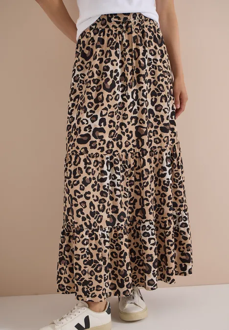 Vrouw draagt een lange, soepel vallende rok met luipaardprint, wit topje en sneakers.