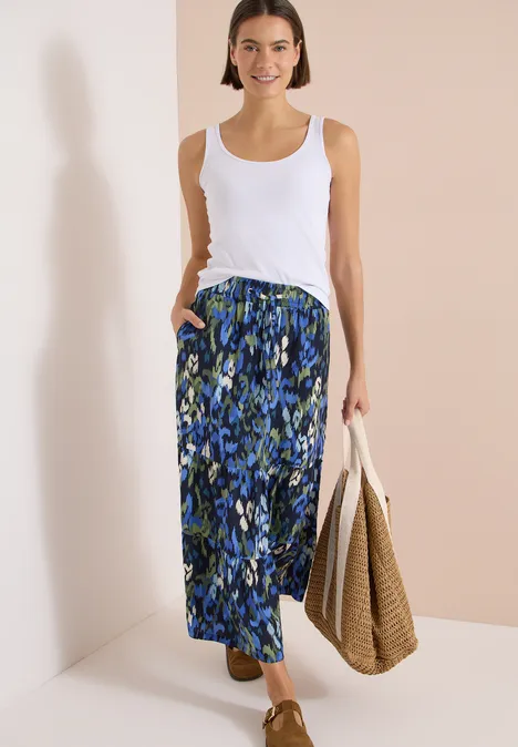 Maxirock mit Volants und Print urban dark blue Dame trägt weißes Top, blauen gemusterten Maxirock und hält eine geflochtene Tasche.