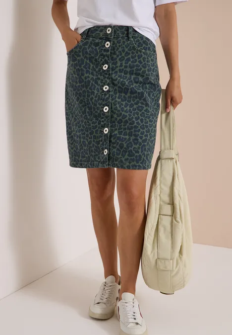 Femme porte une jupe midi boutonnée, baskets blanches et sac fourre-tout beige.