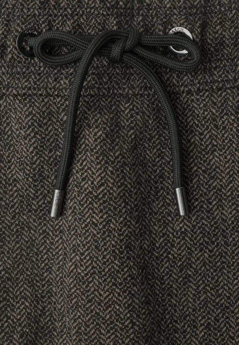 Close-up van een bruin visgraatbroek met zwarte koordsluiting in de taille.