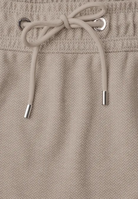 Beige herringbone-stof met trekkoord en metalen uiteinden in de taille van een kledingstuk