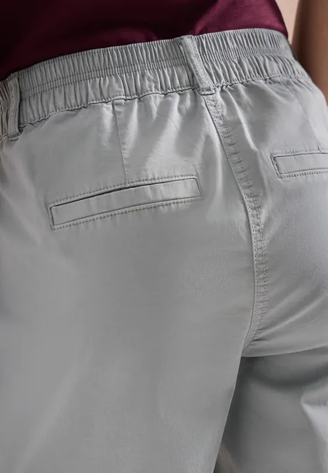 Een persoon draagt een grijze broek met elastische taille en paspelzakken aan de achterkant.