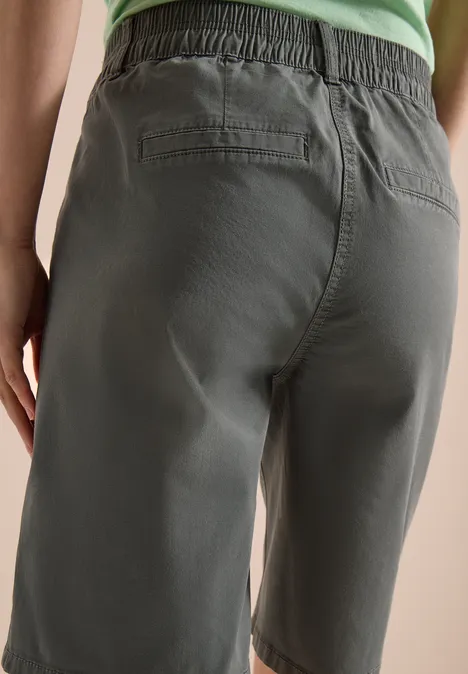 Rückansicht einer Person in olivgrünen Bermudashorts und grünem Top.