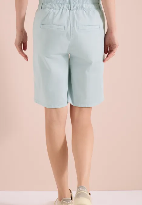 Achteraanzicht van een persoon met lichtblauwe bermudashorts en witte sneakers.