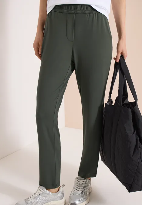 Personne porte un pantalon droit olive taille élastique, baskets blanches et tote bag noir.
