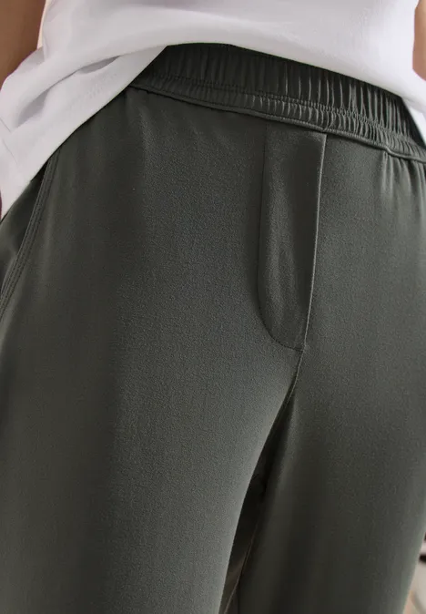 Gros plan sur un pantalon vert foncé taille élastique avec poche latérale, porté avec un haut blanc.