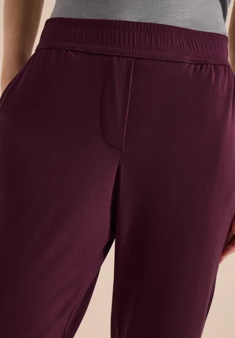Gros plan sur un pantalon de jogging bordeaux avec taille élastique et poches latérales.