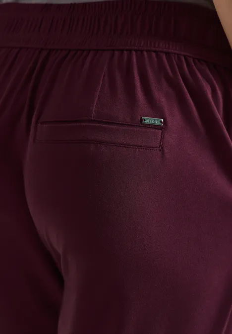 Person portant un pantalon de jogging bordeaux avec taille élastique et poche zippée à l’arrière.