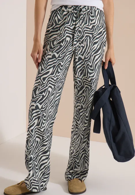 Pantalon large à motif zèbre, haut blanc, sac bleu foncé et chaussures confortables.