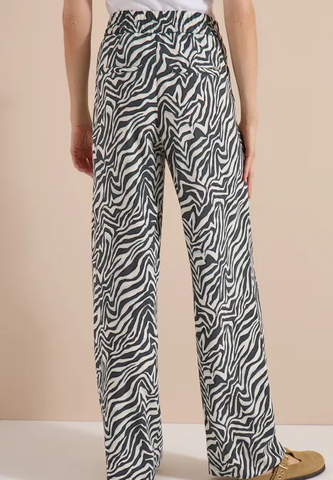 Femme de dos portant un pantalon large à imprimé zèbre noir et blanc sur fond beige.