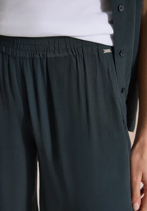 High Waist Wide Leg Hose im Loose Fit palm breeze green Detailansicht: locker sitzende, dunkelgrüne Hose mit elastischem Bund, weißes Top und dunkelgrüne Jacke.