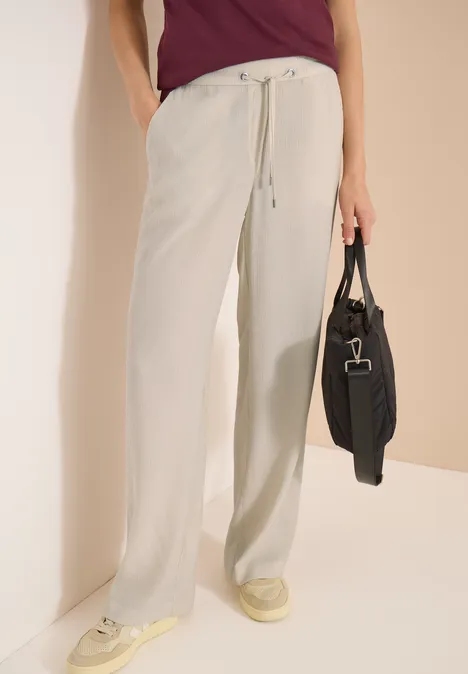 High Waist Straight Leg Hose im Loose Fit grain beige Person trägt helle, weite Leinenhose mit Tunnelzug, cremefarbene Sneaker und hält schwarze Tasche.