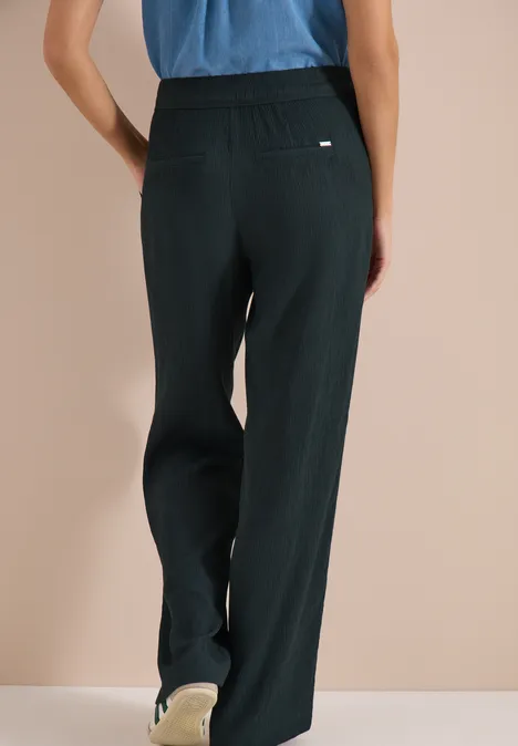 High Waist straight legs broek in Loose Fit palm breeze green Achteraanzicht van een persoon met wijde, donkergroene broek en blauw T-shirt tegen neutrale achtergrond