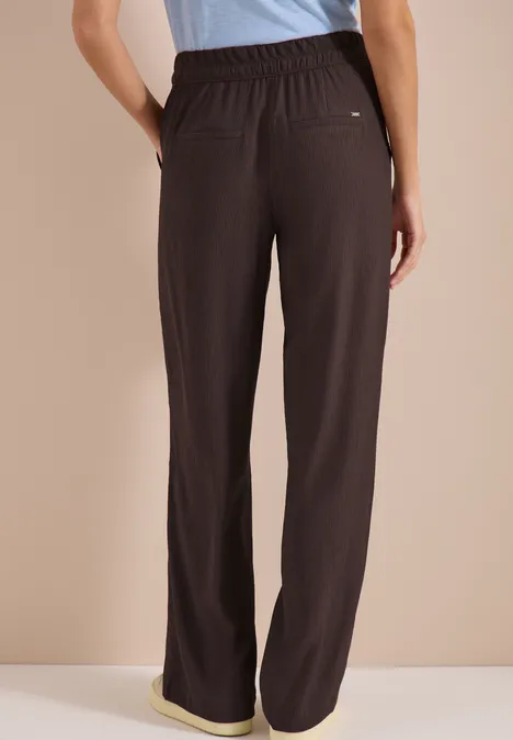 Achteraanzicht van een persoon met een losse bruine broek met elastische taille.