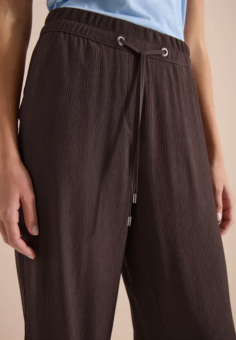 Close-up van een persoon in een bruin, gestructureerd broek met trekkoord en lichtblauw shirt.