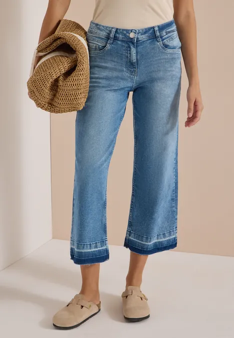Straight Leg Jeans mit frasigem Saum light blue washed Person trägt weite, knöchellange Jeans mit Umschlag, beiges Top, Schlupfschuhe und hält Strohhut.