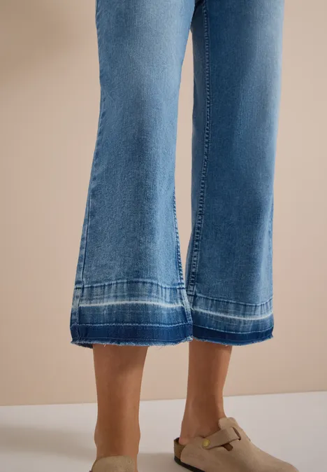 Straight Leg Jeans mit frasigem Saum light blue washed Frau trägt weite blaue Jeans-Culottes mit Ziernähten und beigefarbenen Mules mit Schnalle.