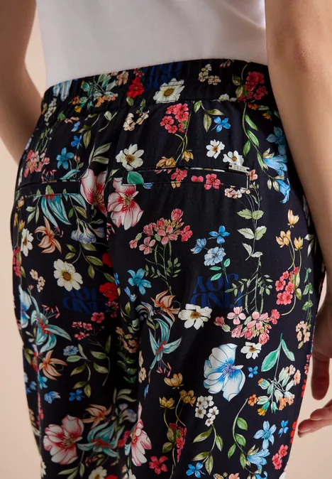 Rückenansicht einer Person in schwarzer Hose mit buntem Blumenmuster.