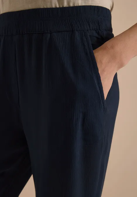 Dunkelblaue, lockere Hose mit elastischem Bund und Seitentasche, Hand in der Tasche.