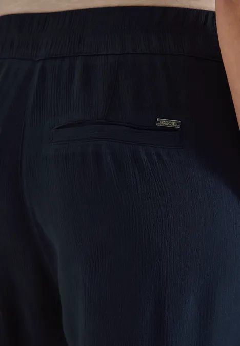 Rückansicht einer dunkelblauen, strukturierten Hose mit elastischem Bund und Reißverschlusstasche am Gesäß.