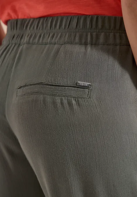 Nahaufnahme einer Person in olivegrünen, leicht strukturierten, elastischen Hosen mit Gesäßtasche.