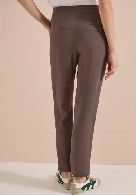 Achteraanzicht van een persoon in een bruine broek en witte sneakers met groene strepen.