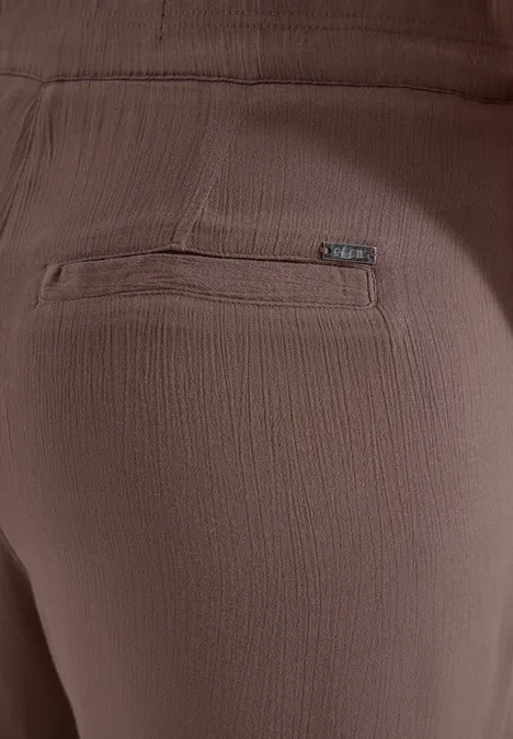 Close-up van een bruine broek met gestructureerde stof en een ritssluiting op de achterkant.