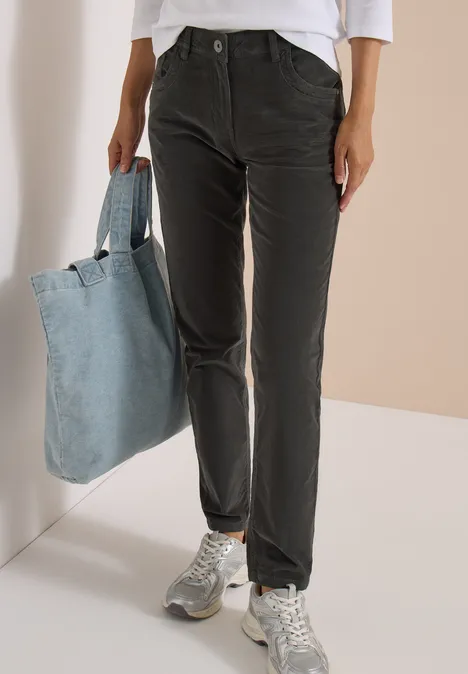 Frau in schwarzer Cordhose, weißem Oberteil, silbernen Sneakern und großer blauer Jeans-Tasche.