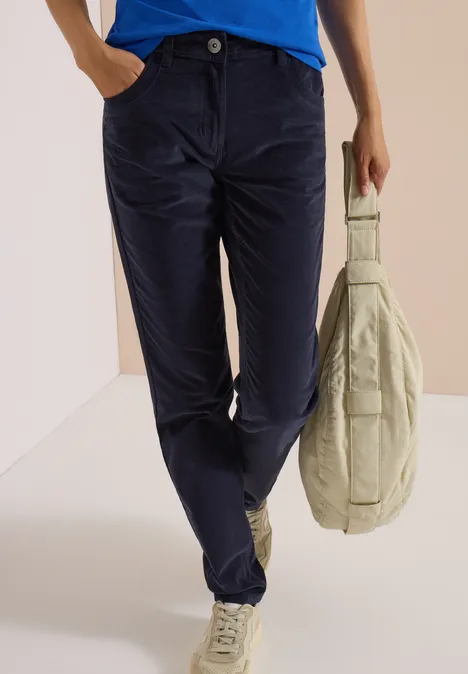 Eine Person trägt dunkelblaue Cordhose und weiße Sneaker, hält eine helle Tasche.