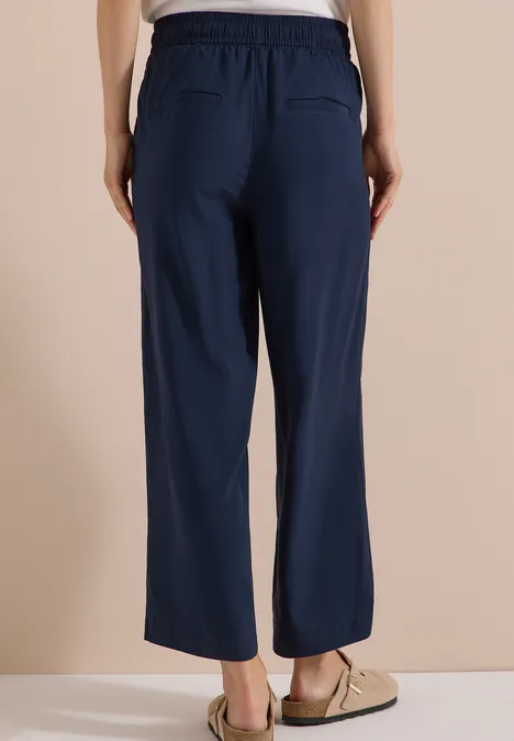 Person von hinten in lockeren, marineblauen Freizeithosen mit Gummibund und Taschen, trägt Sandalen.