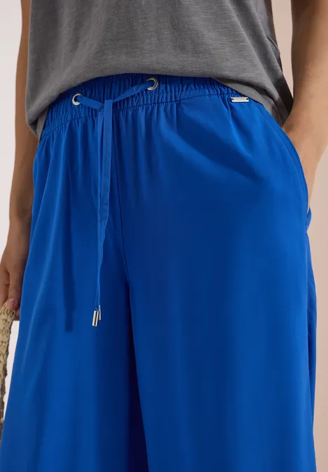 Hose aus knallblauem, fließendem Stoff mit weitem Bein und Kordelzug, kombiniert mit grauem Oberteil.