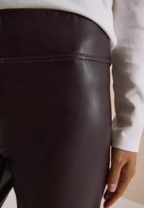 Enge schwarze Lederleggings mit einem weißen Oberteil, Hand an der Seite.