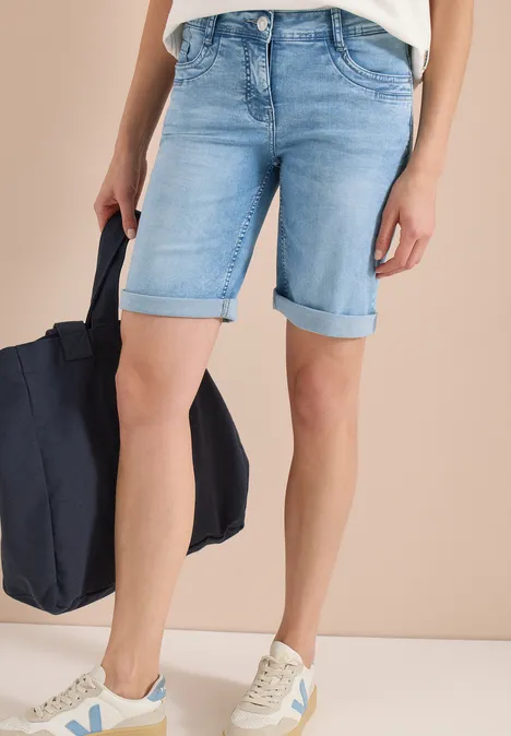 Persoon draagt lichtblauwe jeansshort met omgeslagen zoom, witte sneakers en houdt een donkerblauwe tas vast.