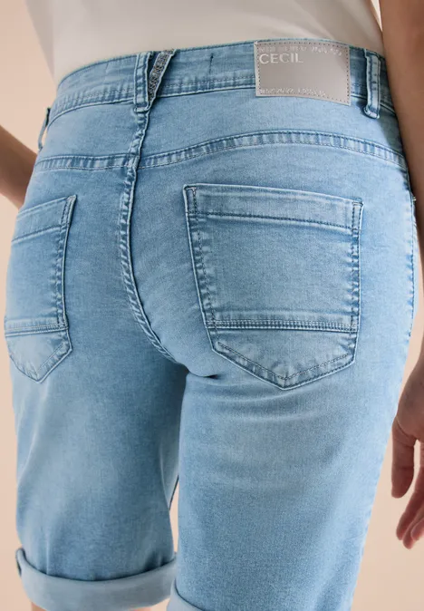 Close-up van de onderrug van een persoon in lichtblauwe, opgerolde spijkerbroek.