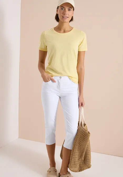 Vrouw in geel T-shirt, witte driekwartbroek en gevlochten tas.