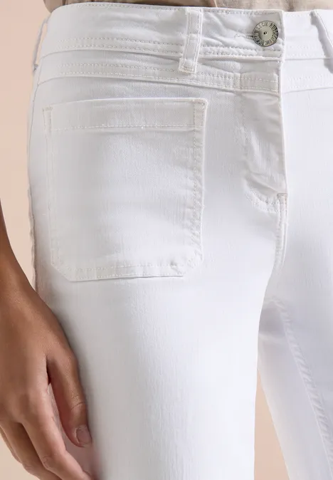 Close-up van een witte, nauwsluitende jeans met voorzak en hand op het bovenbeen.