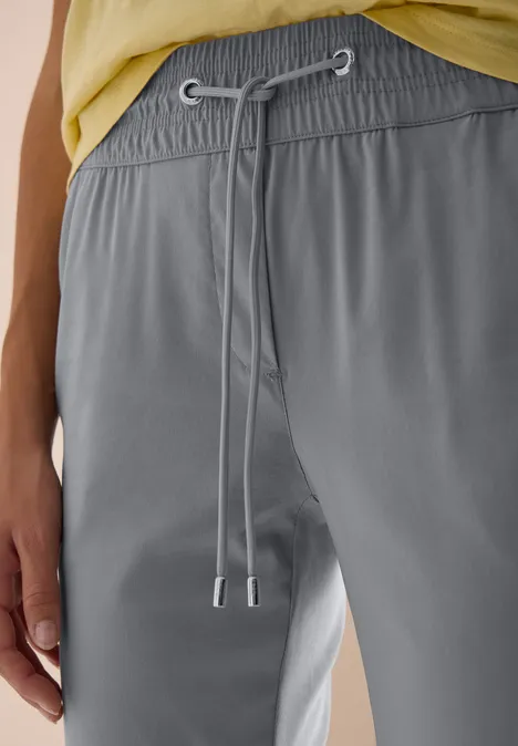Grijze vrijetijdsbroek met elastische taille en koordsluiting, gedragen met een lichtgele top.