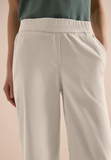 Hose aus beigem Baumwollstoff mit elastischem Bund und seitlichen Taschen, lässig und bequem.